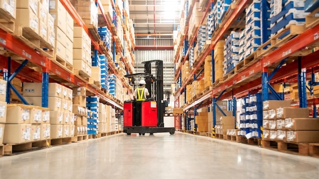 Worker using a forklift in an isle of a full warehouse