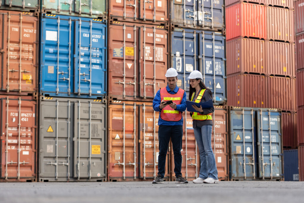 Foreman worker and female industrial engineer checking loading containers at terminal port transport goods.
