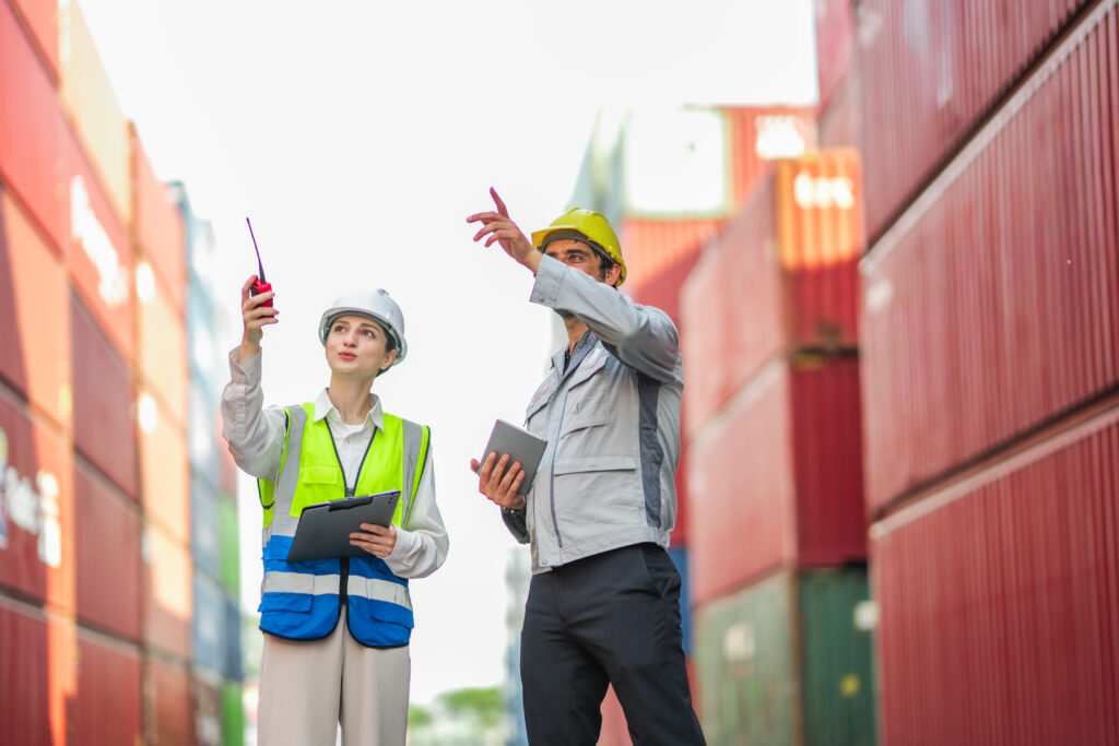 Logistics workers inspecting shipping containers in cargo yard using digital tools