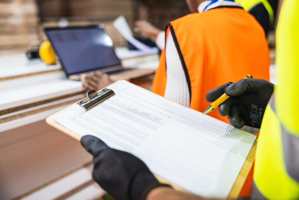 Hand in safety glove holding pen and clipboard with checklist, verifying inventory data