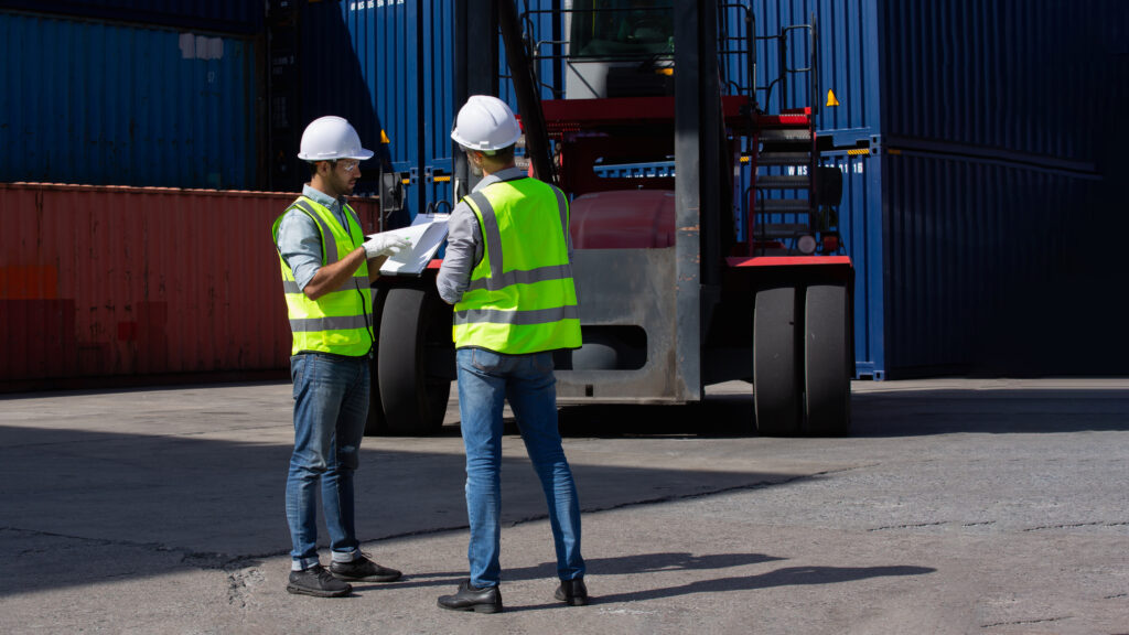 Serious business unfolds beside powerful forklift within vast outdoor shipping container yard as two professionals examine logistics paperwork during critical inspection assessment.