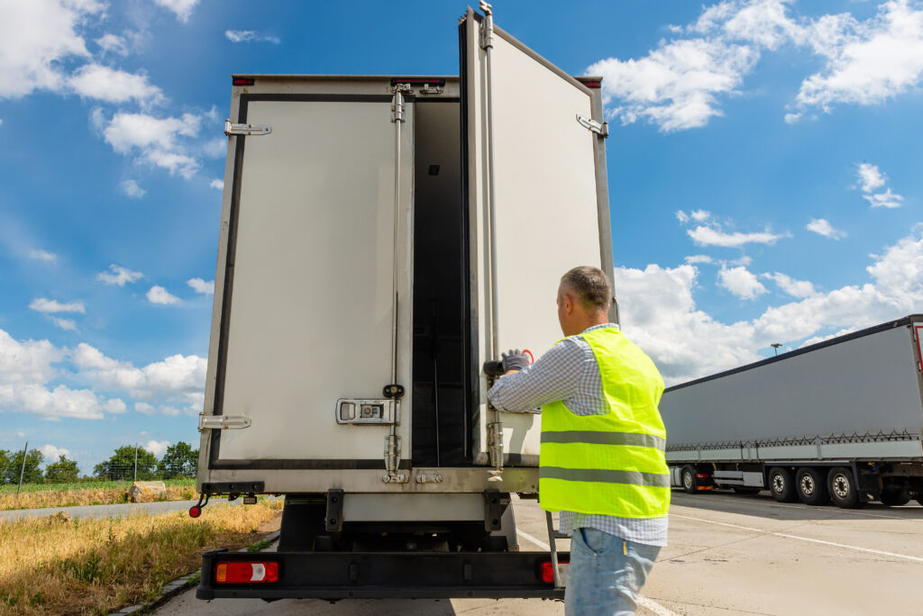 Driver standing near open cargo doors of reefer truck