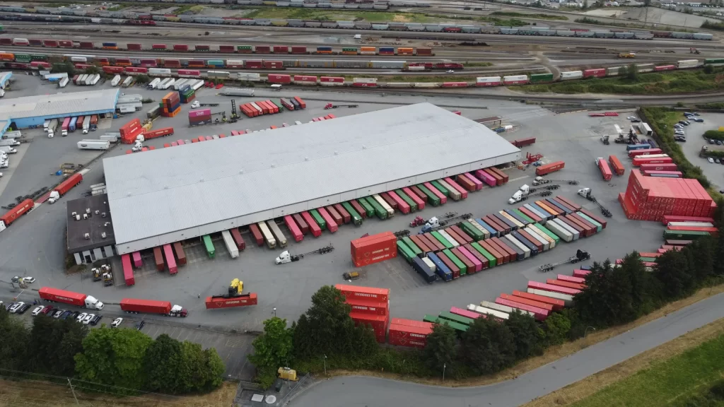 Aerial view of WTC Group's Kingsway intermodal terminal with shipping containers, truck trailers, rail lines, and warehouse loading docks.
